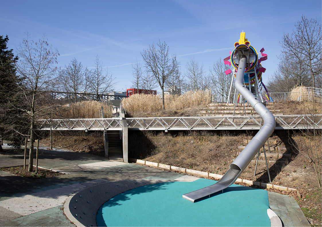 Photo en plan large du jardin du Dragon au Parc de la Villette à Paris. Une aire de jeux pour enfants avec une structure design de dragon colorée qui contient un toboggan.