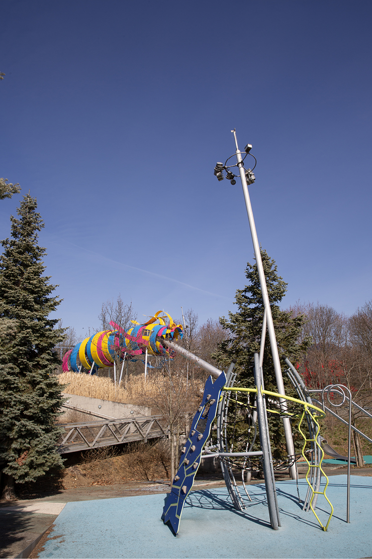 Photographie d'illustration en format portrait du jardin du Dragon au Parc de la Villette à Paris. Une aire de jeux pour enfants avec structure de dragon colorée qui contient un toboggan.